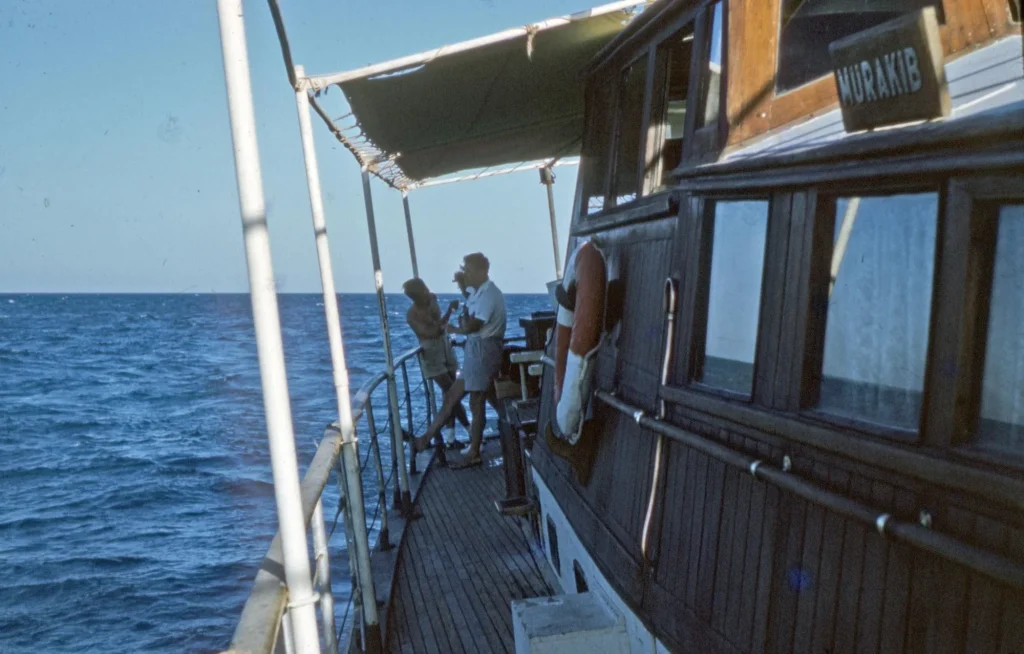 Two people standing on a wooden boat deck at sea on a sunny day, showing a relaxed boat day setting