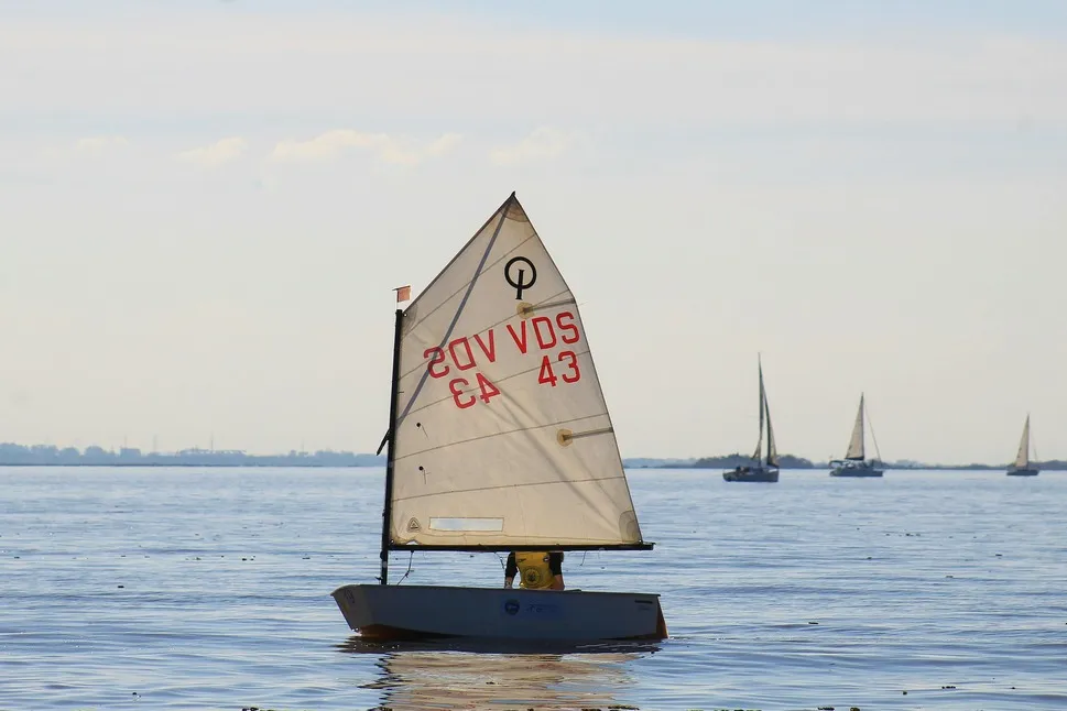Small sailing dinghy on calm water with a single sail raised