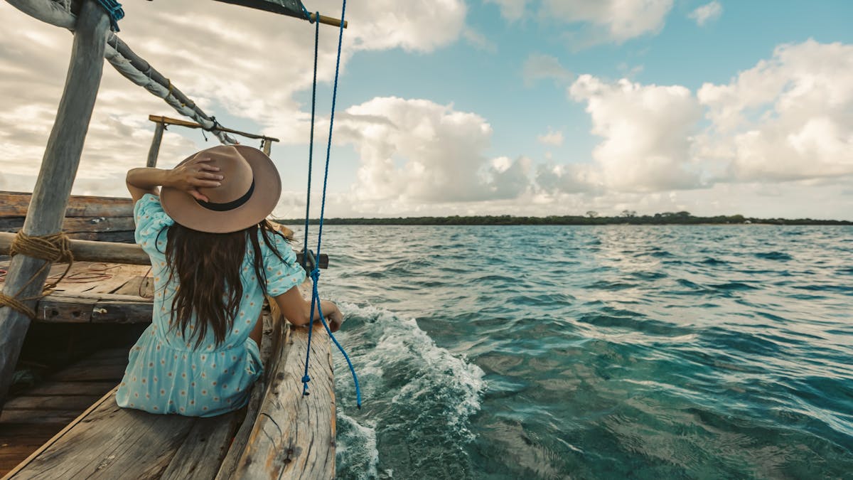 A woman in a hat sitting on a wooden boat at sea